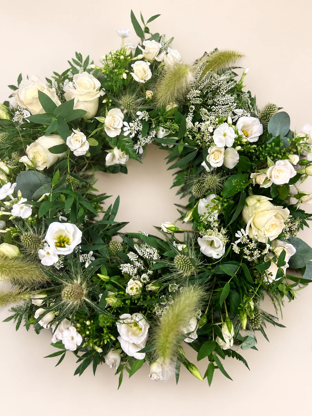 Natural white funeral wreath with cream roses, white flowers, grasses and loose green foliage