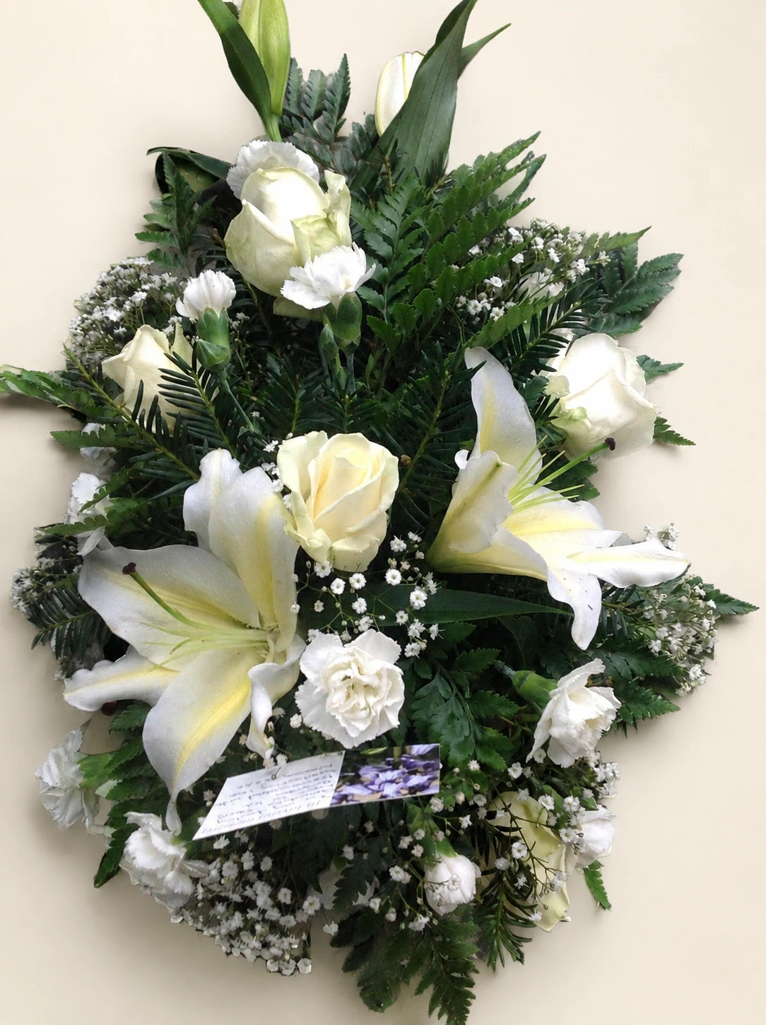 Close view of a white lily and cream roses with gypsophila in a single-ended funeral spray