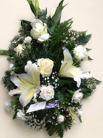 Close view of a white lily and cream roses with gypsophila in a single-ended funeral spray