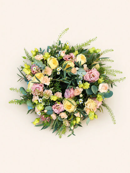Pastel funeral wreath with pale yellow roses, pink flowers, eucalyptus and green foliage