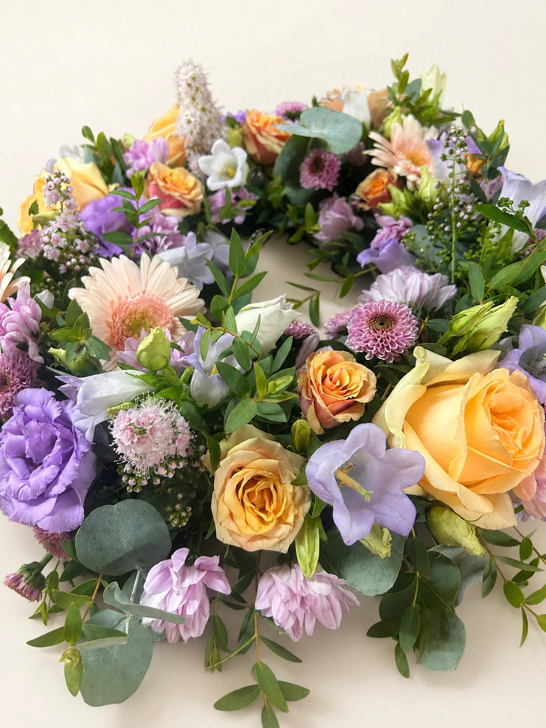 Close view of a pastel wreath with peach roses, lilac flowers, pale pink gerberas and eucalyptus