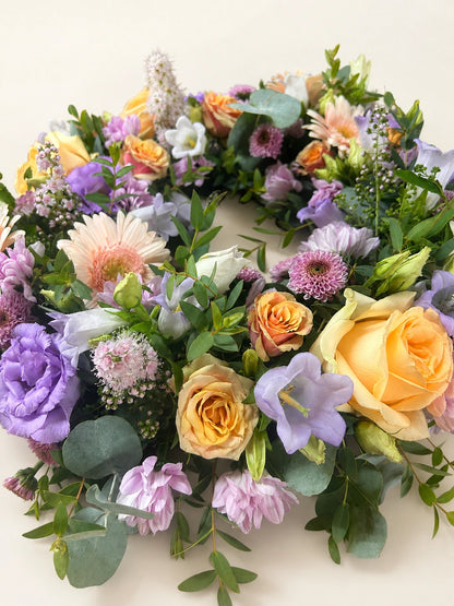 Close view of a pastel wreath with peach roses, lilac flowers, pale pink gerberas and eucalyptus