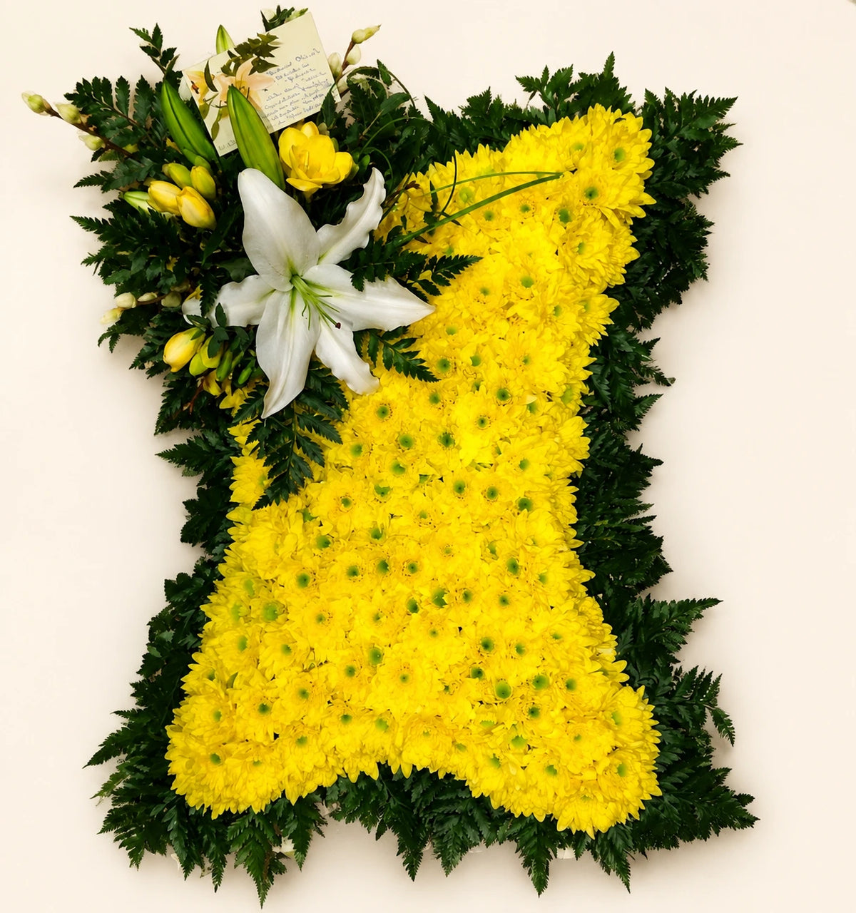 Yellow floral funeral pillow edged with dark green foliage and finished with white lilies