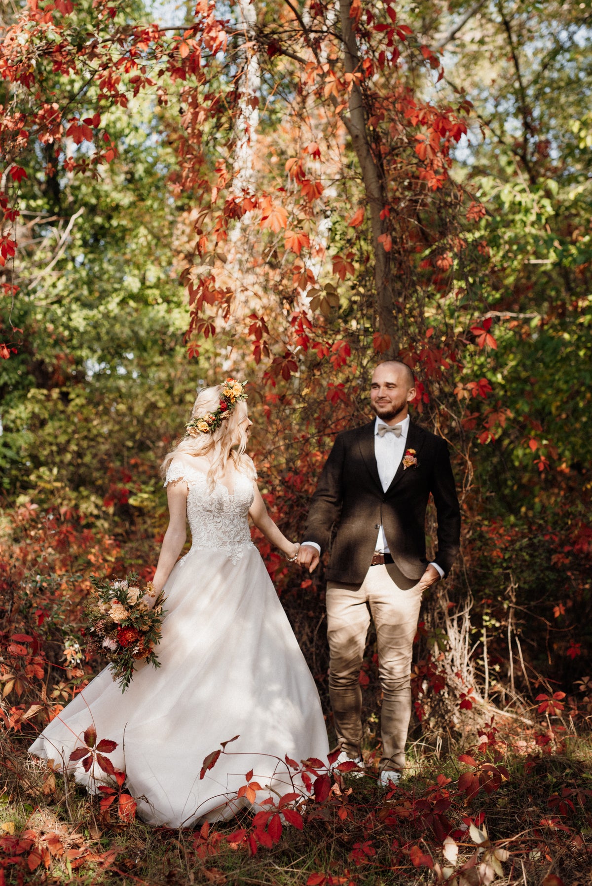 Bride and groom holding hands beneath autumn trees, with an autumn-coloured bridal bouquet.