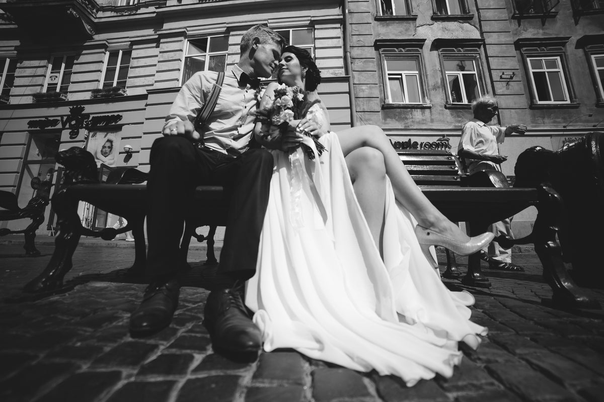 Black and white photograph of a bride and groom seated on a bench with a bridal bouquet.
