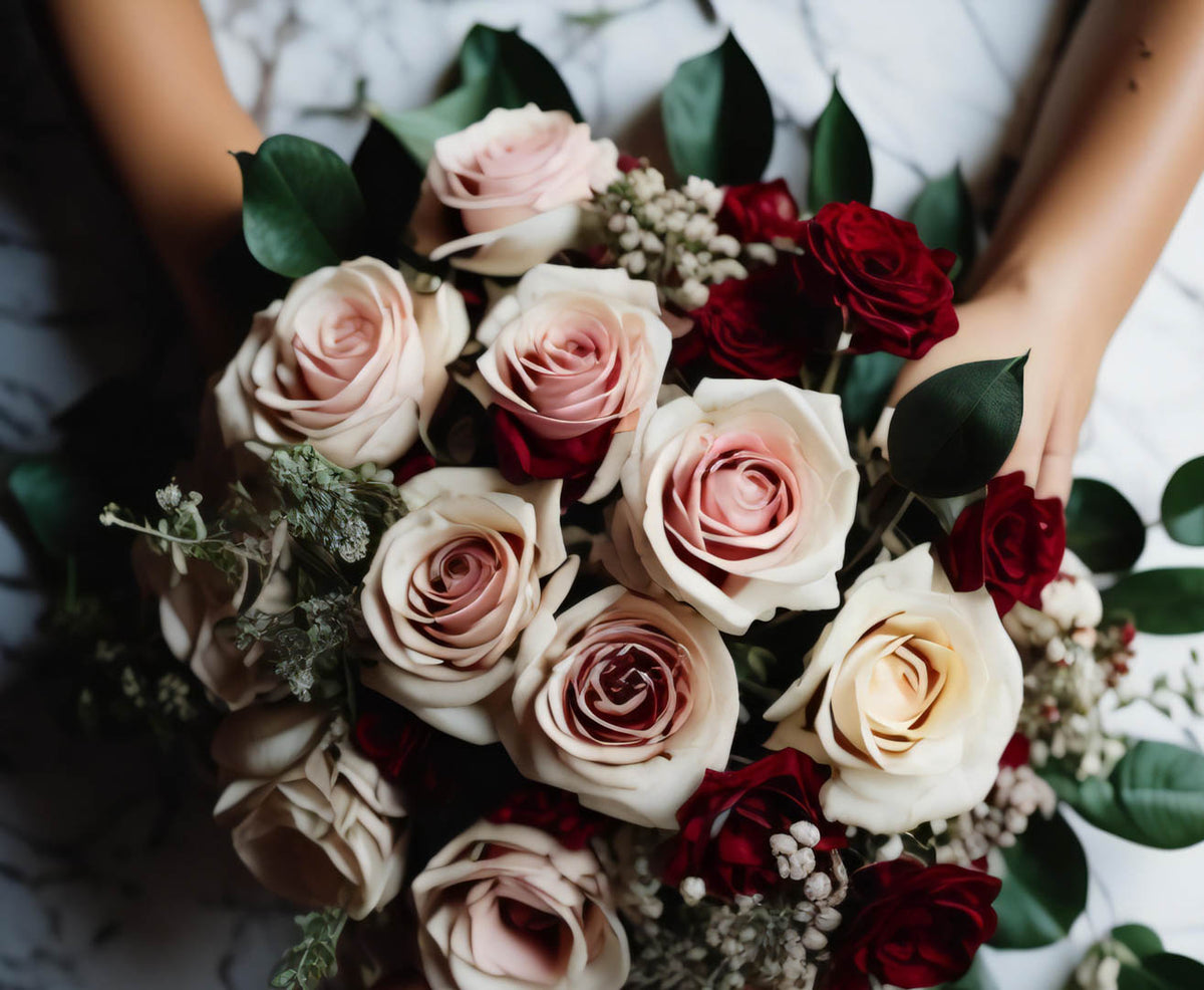 Close-up of a bridal bouquet with blush, cream and burgundy roses and dark green leaves.