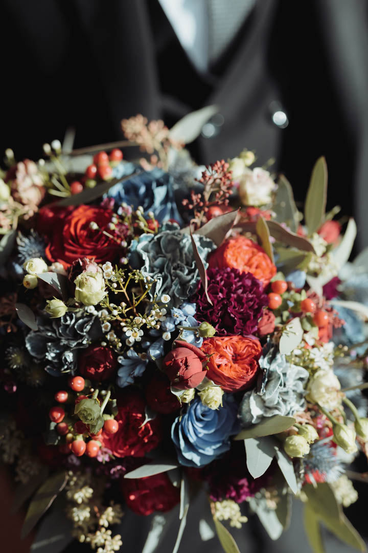 Wedding bouquet with orange and burgundy flowers, blue-grey foliage and small berries.