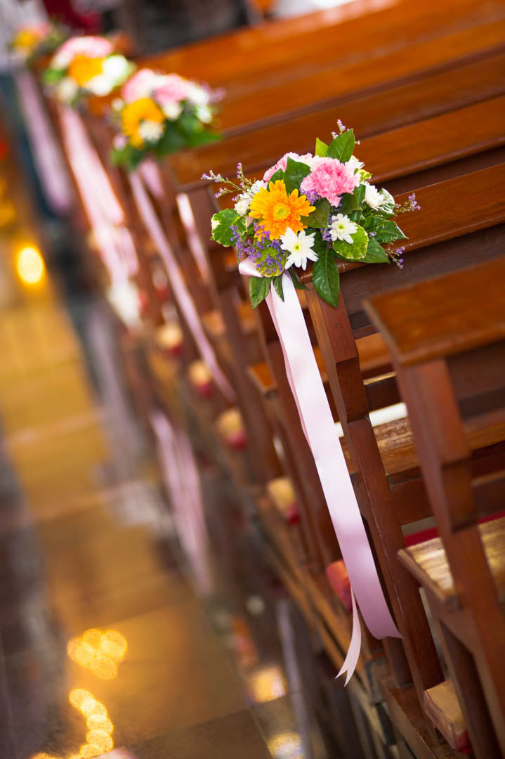 Small yellow, pink and white wedding posies with pink ribbons tied to wooden church pews.