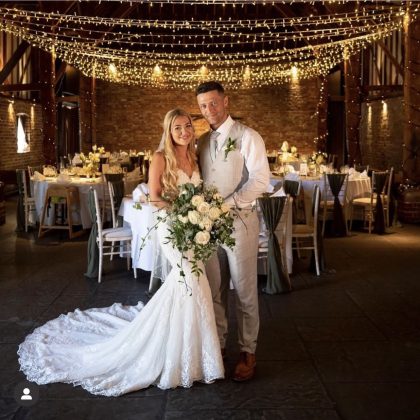 Fern and Simon together at their wedding venue, with a bridal bouquet.