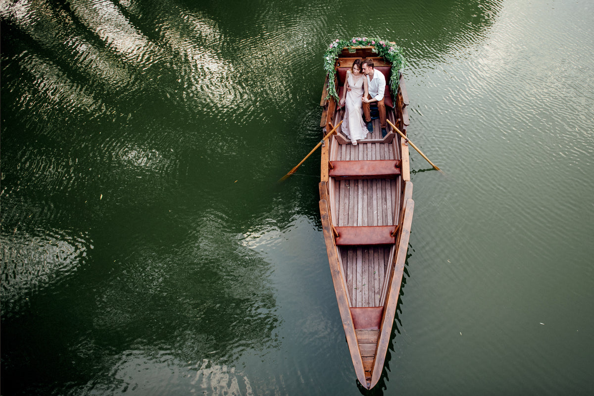 Bride and groom seated in a wooden boat decorated with flowers and greenery.