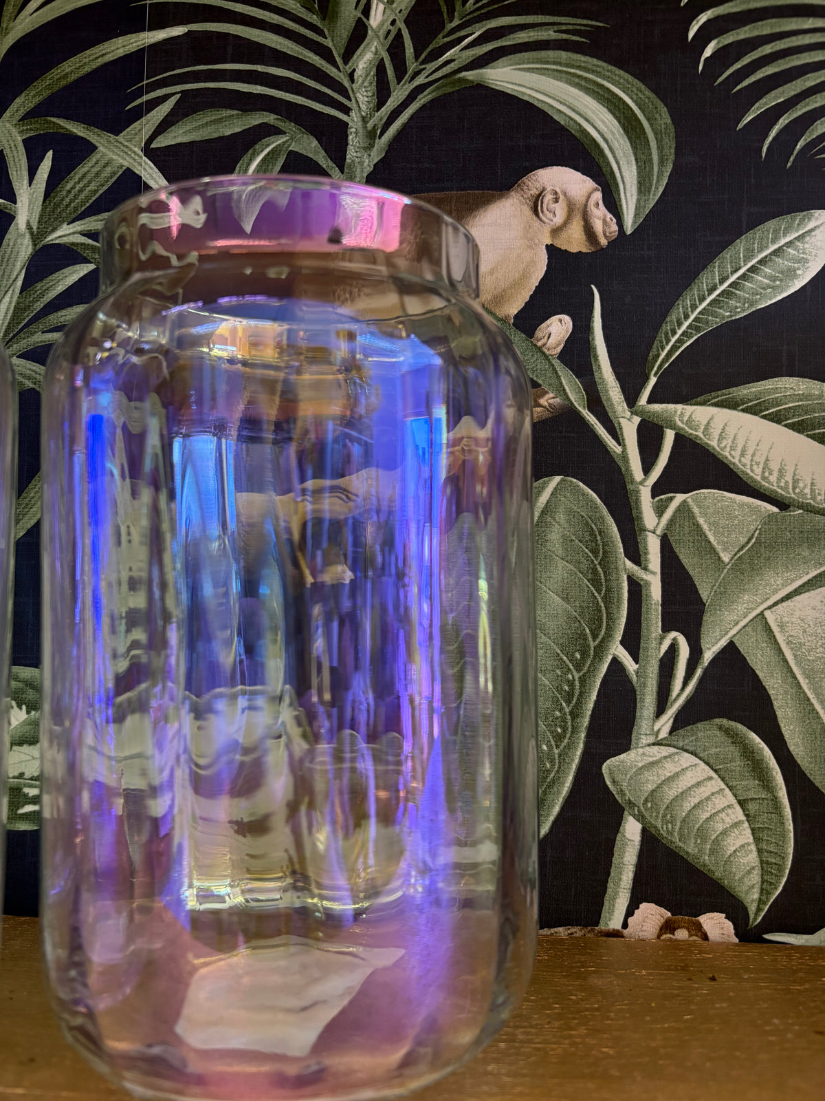 Tall ribbed glass vase with an iridescent blue and lilac sheen, displayed against botanical wallpaper