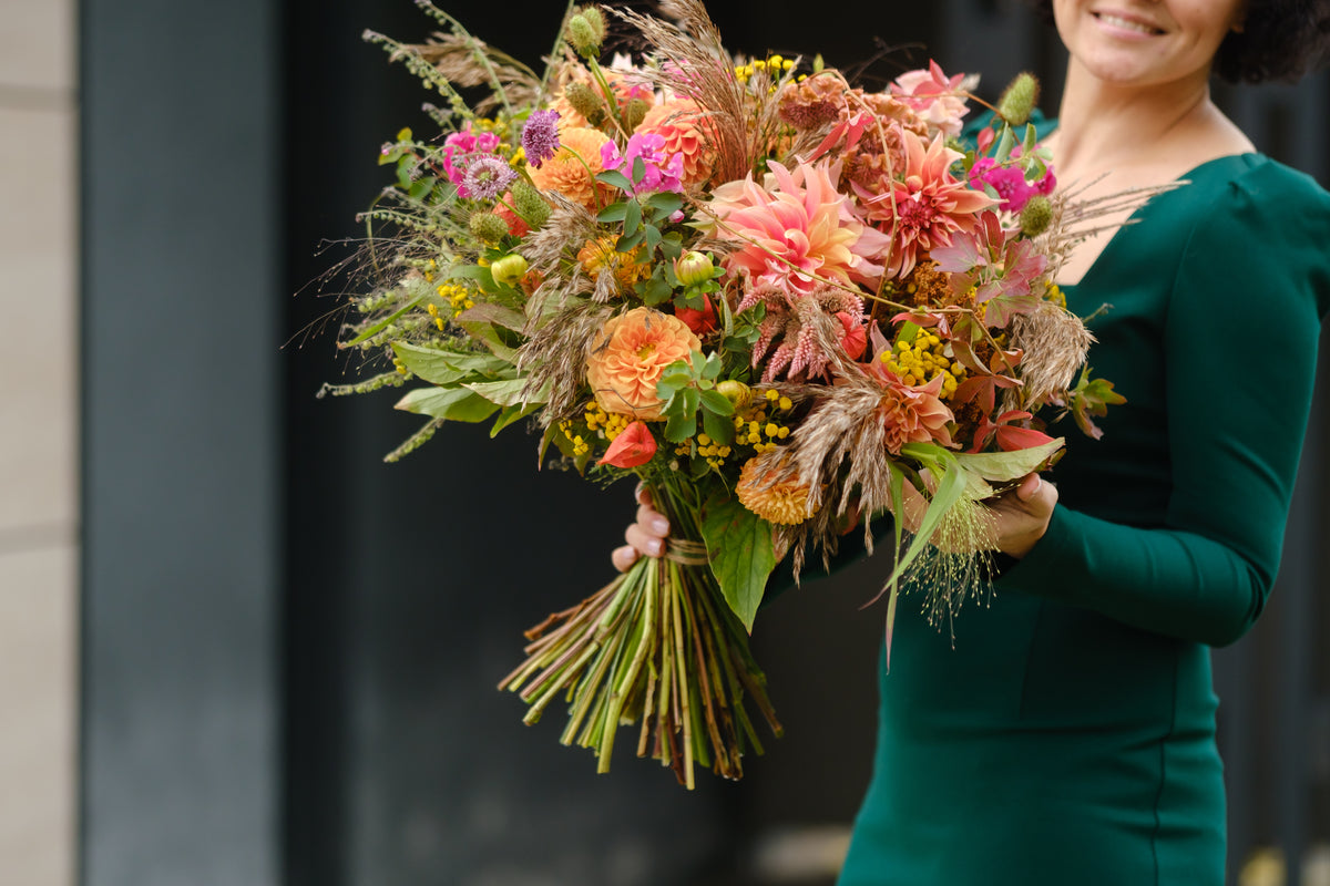 Loose hand-tied bouquet of peach and pink flowers with grasses and green foliage.