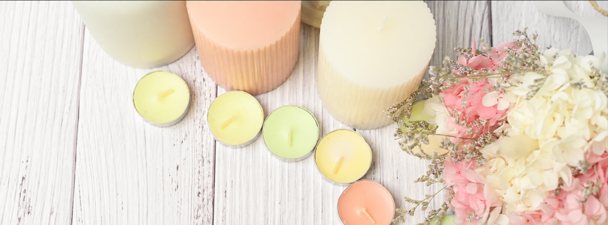 Pastel candles and pink and cream flowers on a pale wooden surface