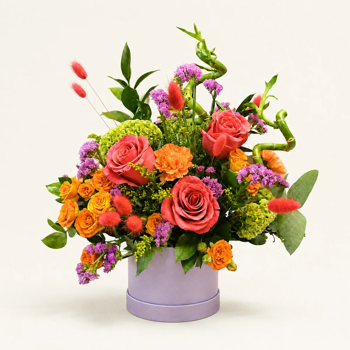 Lotty’s Signature Hatbox with coral roses, orange spray roses, green celosia and purple statice in a lilac hatbox