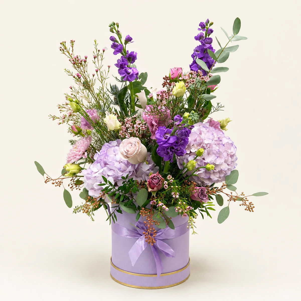 Lilac hydrangeas, purple stock and pale roses with eucalyptus in a tall lilac Signature Hatbox with a ribbon bow