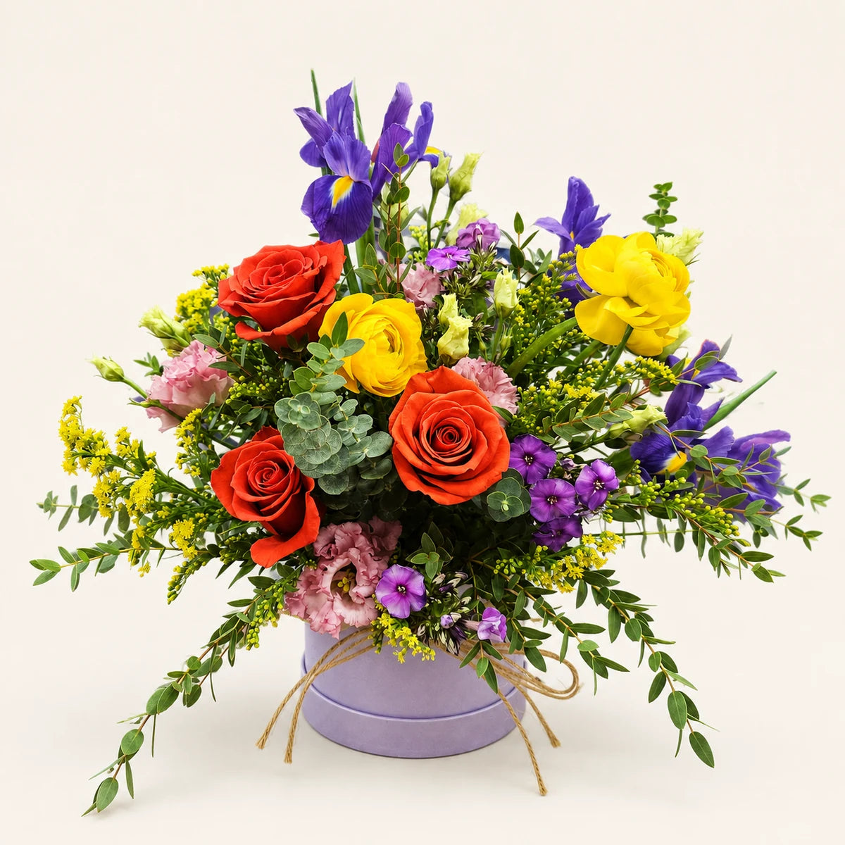 Orange roses, purple irises and yellow ranunculus with pink flowers and eucalyptus in a lilac Signature Hatbox