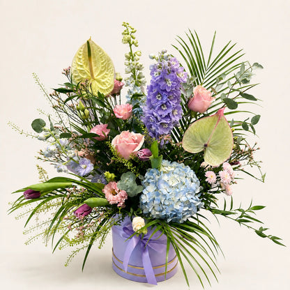 Pastel Signature Hatbox with blue hydrangea, lilac delphinium, pink roses and pale anthuriums in a ribboned lilac box