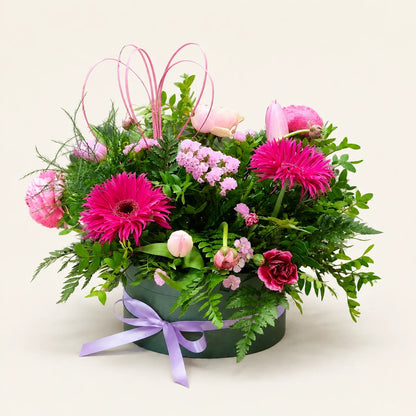 Pink gerberas, tulips and roses with green foliage in a dark green Signature Hatbox tied with a lilac ribbon
