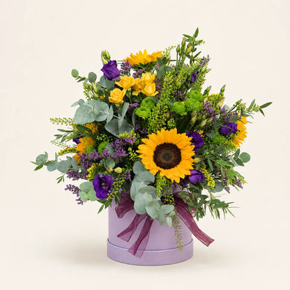 Sunflowers, yellow spray roses and purple lisianthus with eucalyptus in a lilac hatbox tied with a plum ribbon