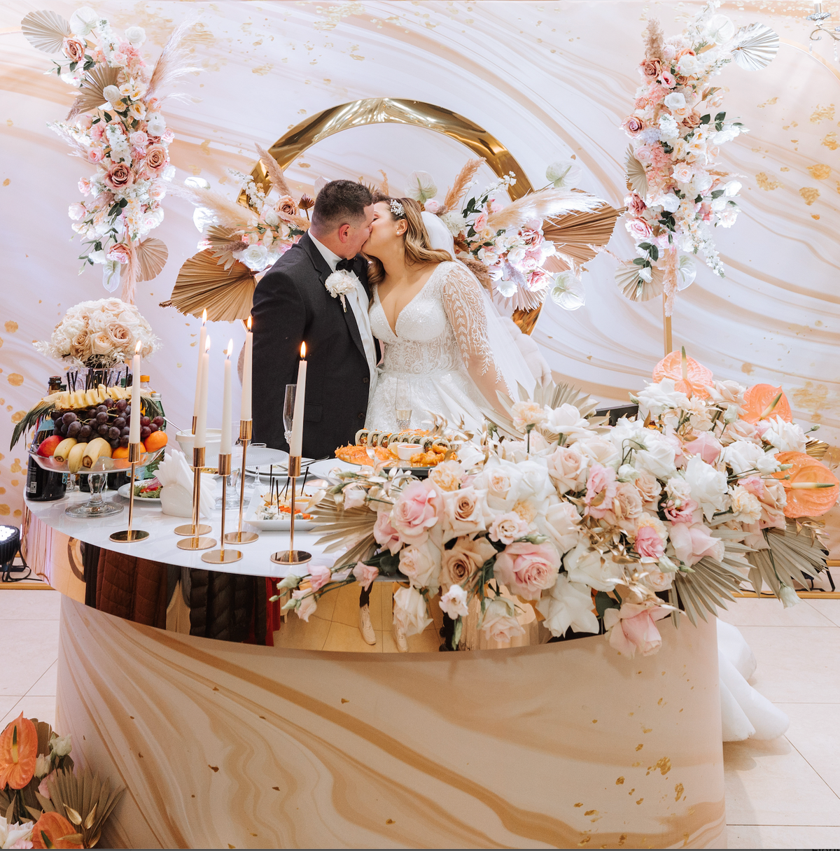 Bride and groom at a reception table decorated with pink flowers and pampas grass.