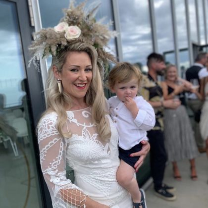 Bride wearing a pampas and dried flower headpiece while holding a young child.