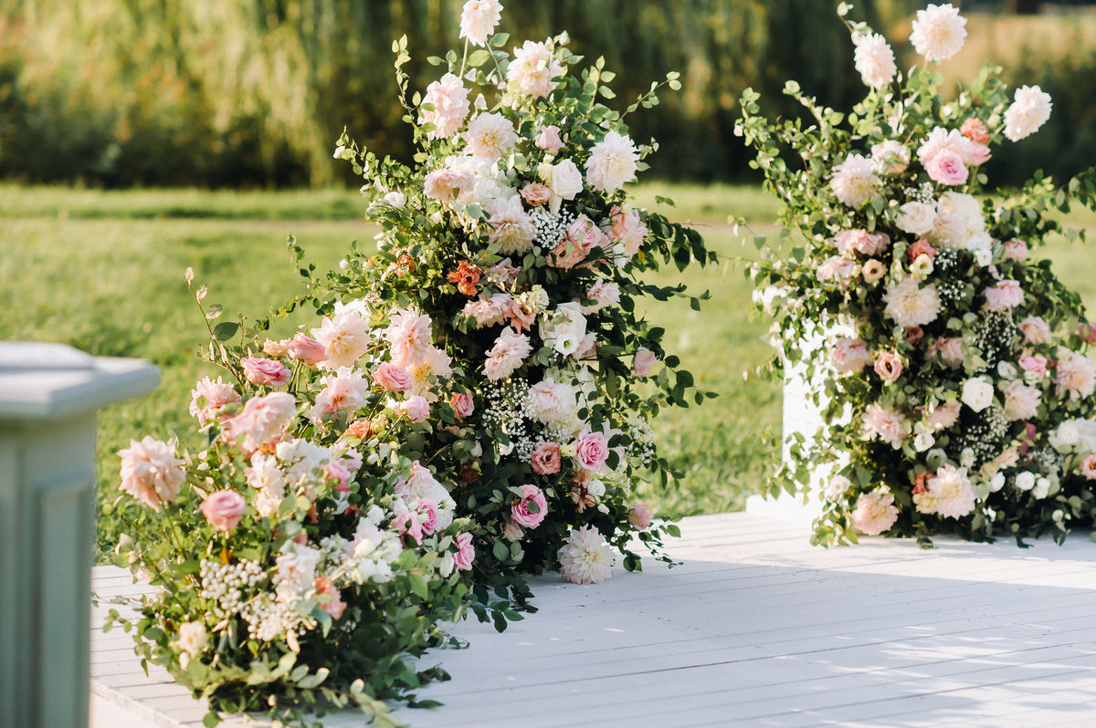 Tall, airy arrangements of pink and white flowers with greenery framing an outdoor wedding ceremony.