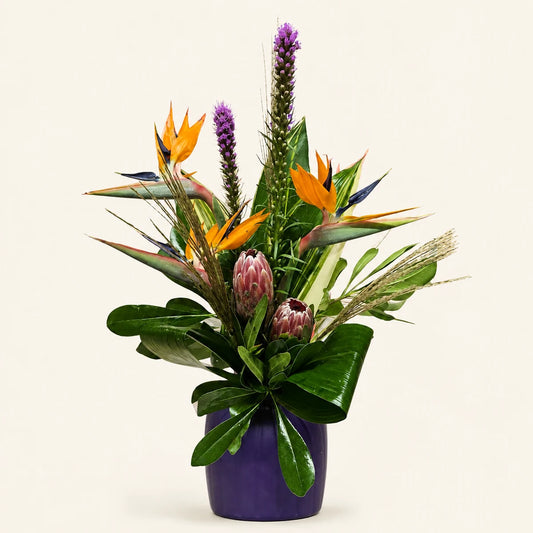 Premium vase arrangement with orange bird of paradise, purple liatris, pink protea and lush foliage in a purple vase