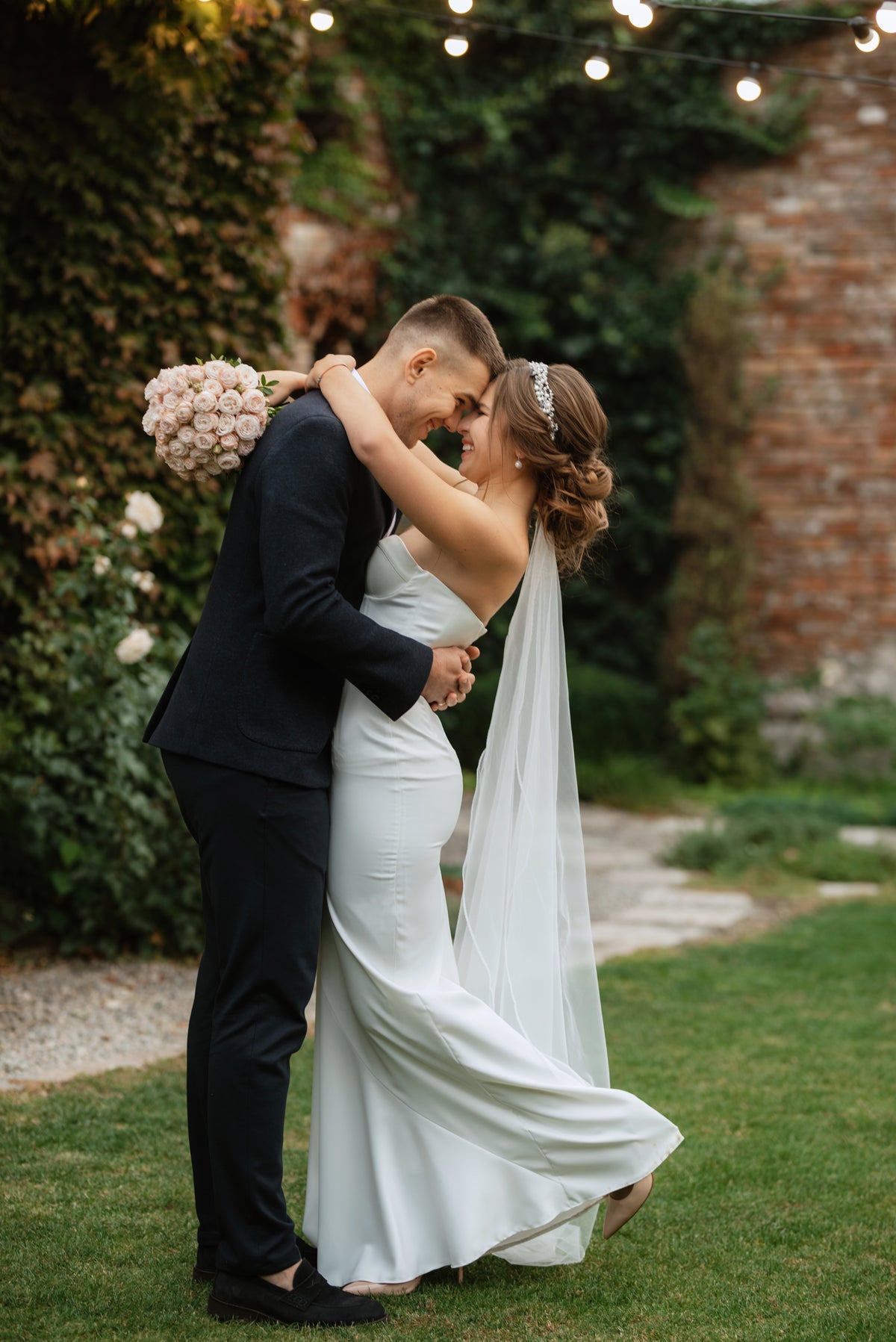 Bride and groom embracing outdoors, with a rounded pale pink rose bridal bouquet.