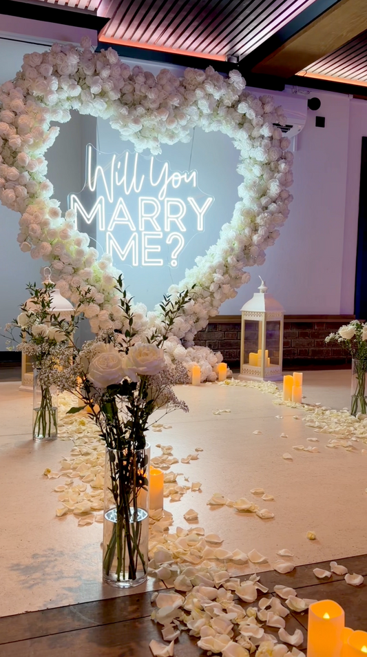White rose heart with an illuminated Will you marry me sign, lanterns and soft candlelight.