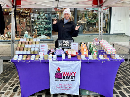 Waxy Beast market stall displaying handmade soy and coconut candles on a purple-covered table