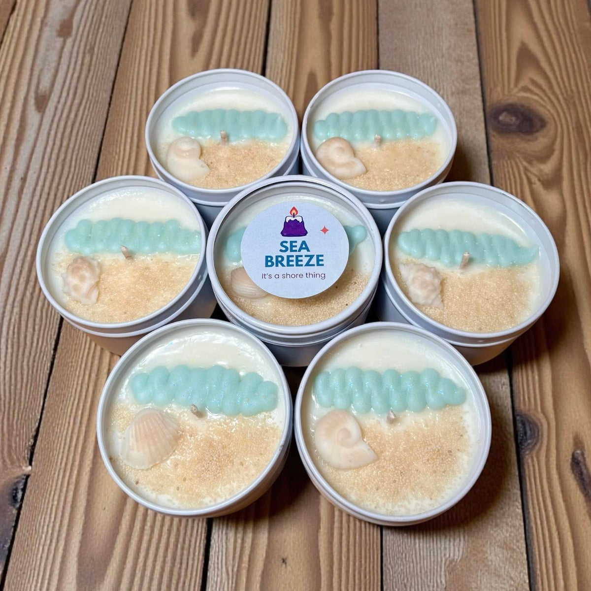Waxy Beast Sea Breeze candles in white tins, decorated with pale blue waves and cream seashells