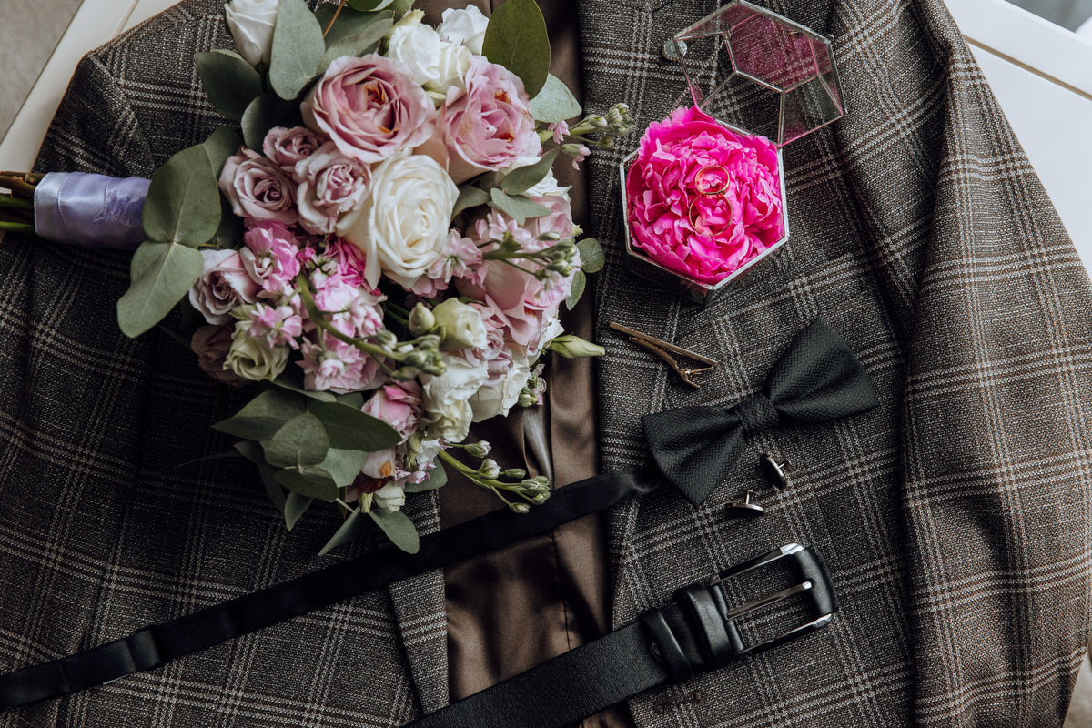 Blush rose wedding bouquet, dark bow tie and ring box arranged on a checked wedding suit.