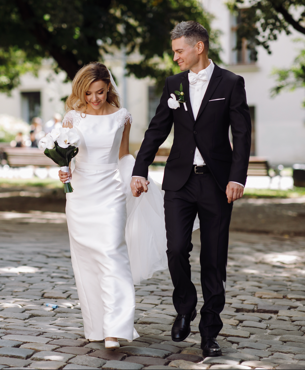 Bride and groom walking together, with a cascading white orchid bridal bouquet and matching white buttonhole.